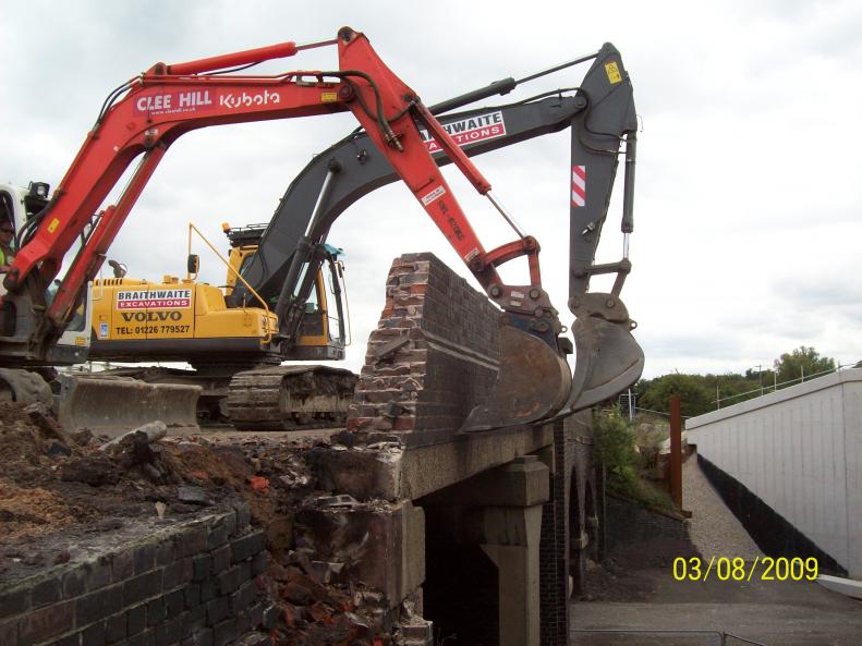 Excavators working together to pull in the parapets